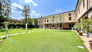 A courtyard with a well-maintained lawn, a classical column, and a building with multiple windows and balconies. - HC Hotel Il Gelso Pontevico (Pontevico)
