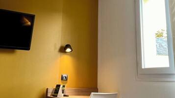 A hotel room with a bed, a desk, a chair, a TV mounted on the wall, and a window.