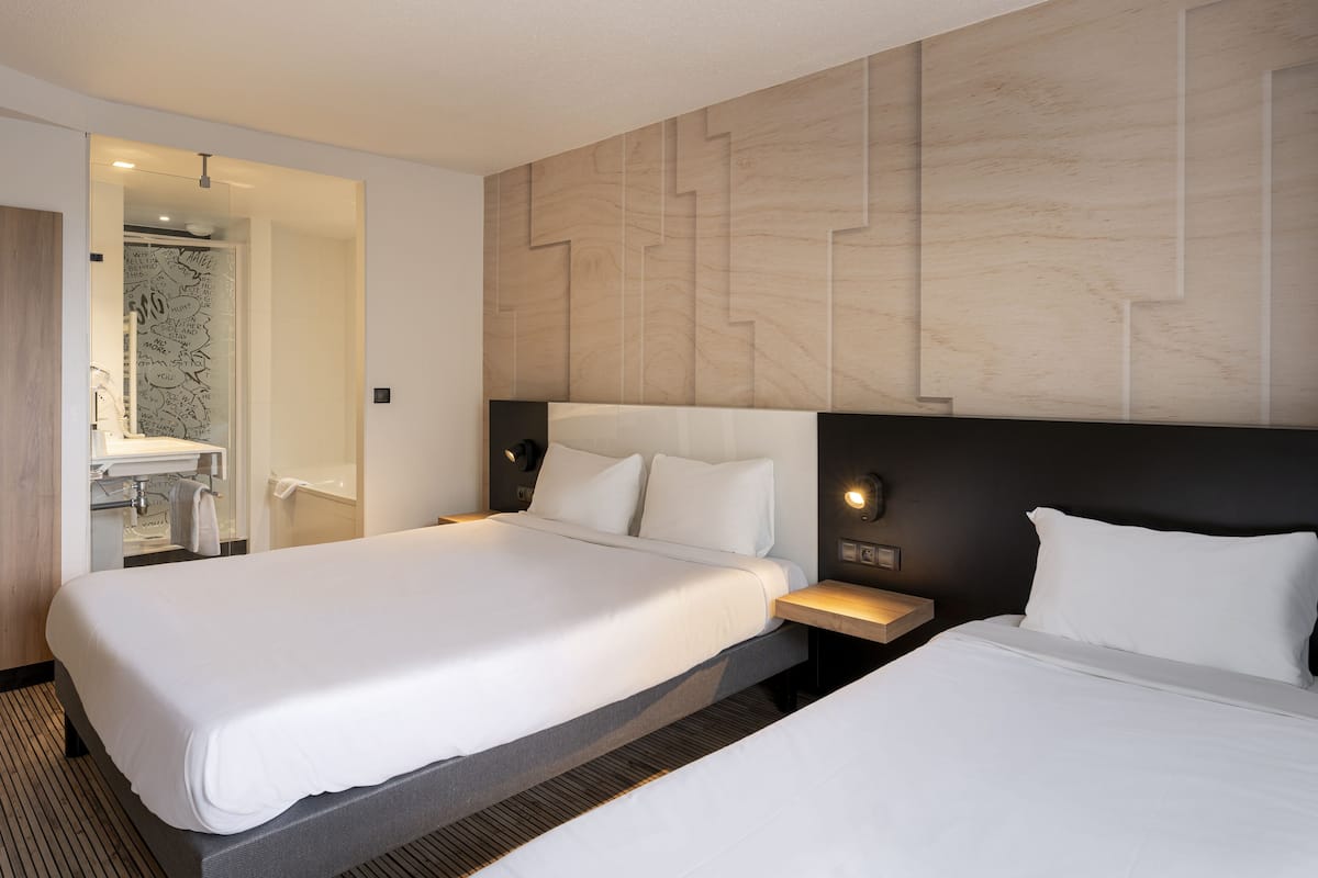 Habitación de hotel con dos camas, un baño y diseño moderno.