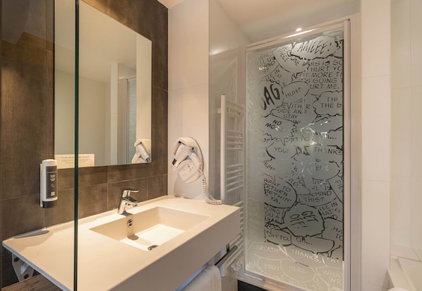 Un baño moderno con un espejo grande, un lavamanos blanco y una cabina de ducha de vidrio con grafiti.