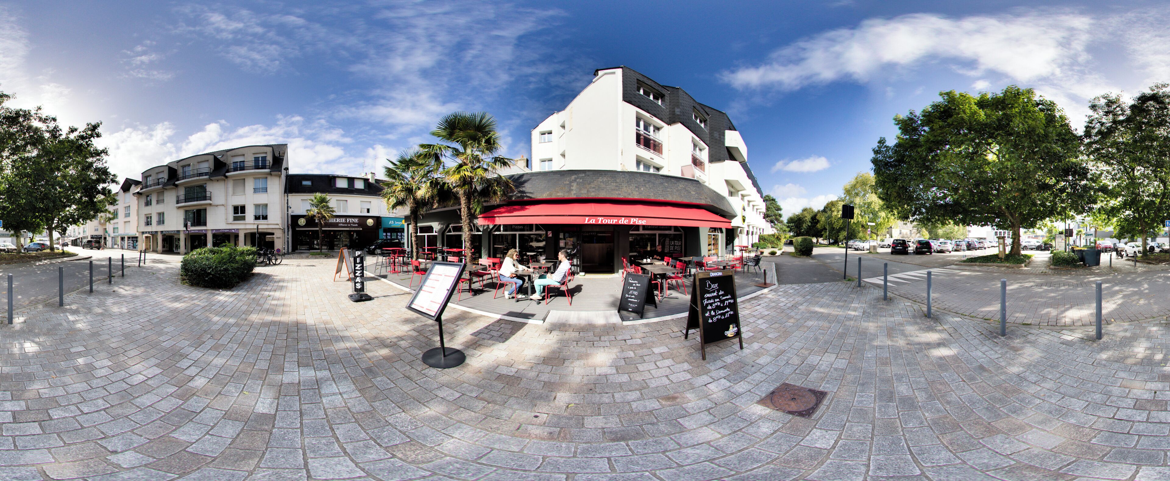 A café with outdoor seating, a red awning, and a signboard.