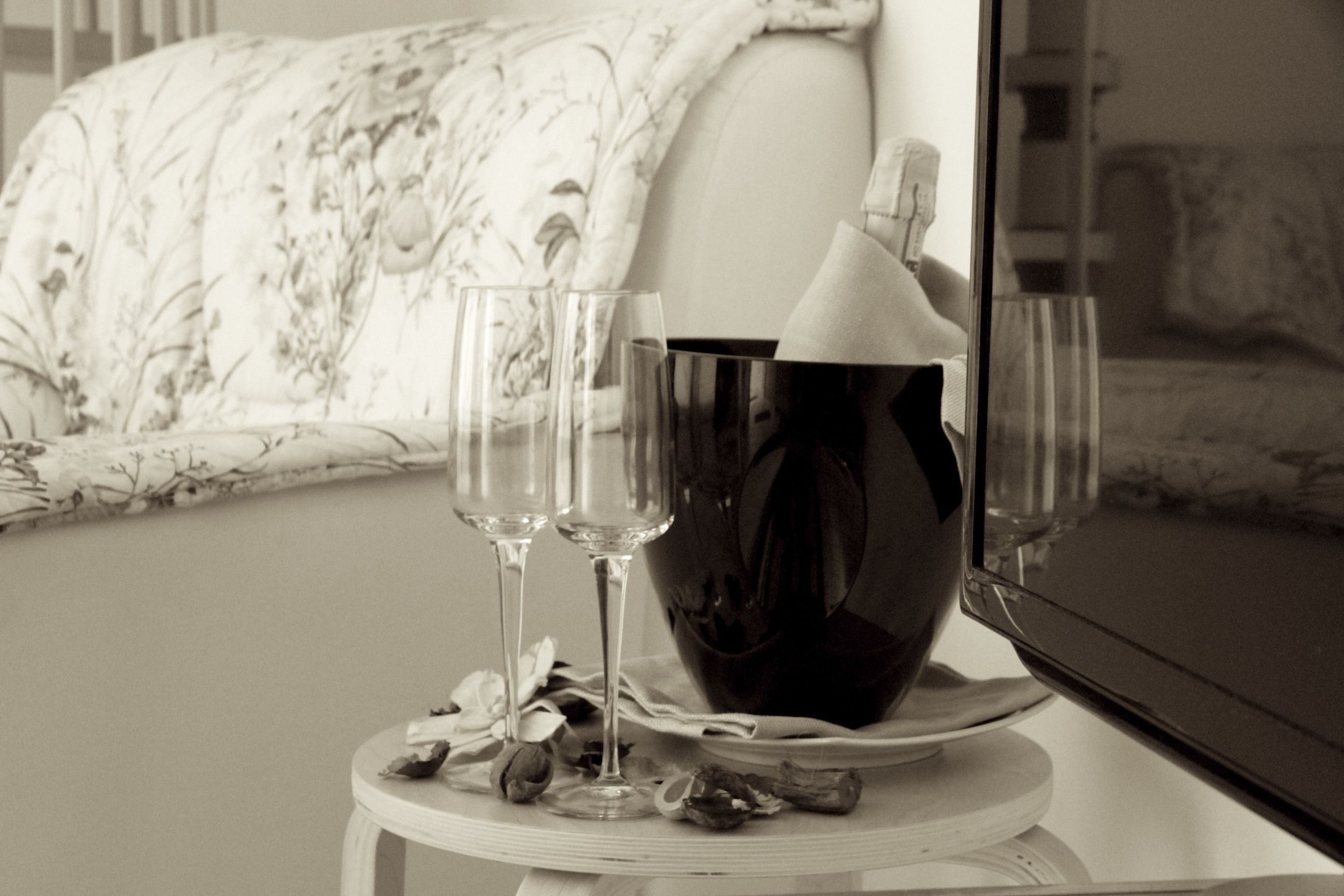 Fotografía en blanco y negro de una habitación con una cama, una mesita de noche con un florero y un televisor.