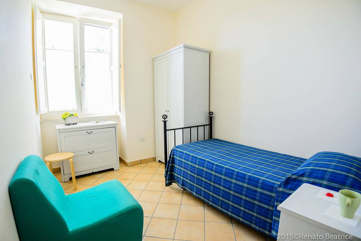 Et lille, rent værelse med en seng, et hvidt skab, et lille bord og et vindue.