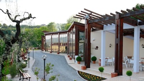 A modern outdoor area with a pergola, seating, and a pathway leading to a building with glass doors. - aCasaMia Wine Resort - Borgo Salella (San Cipriano Picentino)