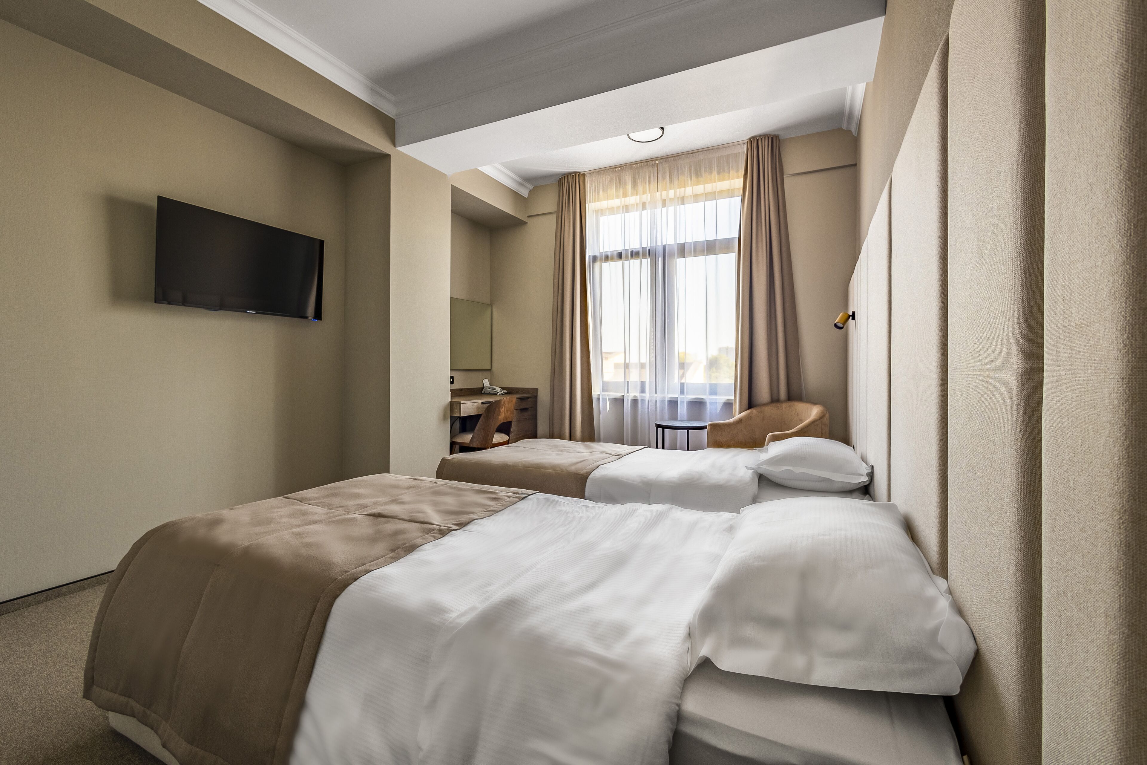 Habitación de hotel con dos camas, un escritorio, una silla, un televisor y una ventana con cortinas.