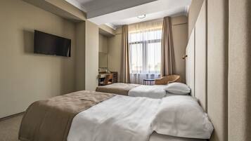 Habitación de hotel con dos camas, un escritorio, una silla, un televisor y una ventana con cortinas.
