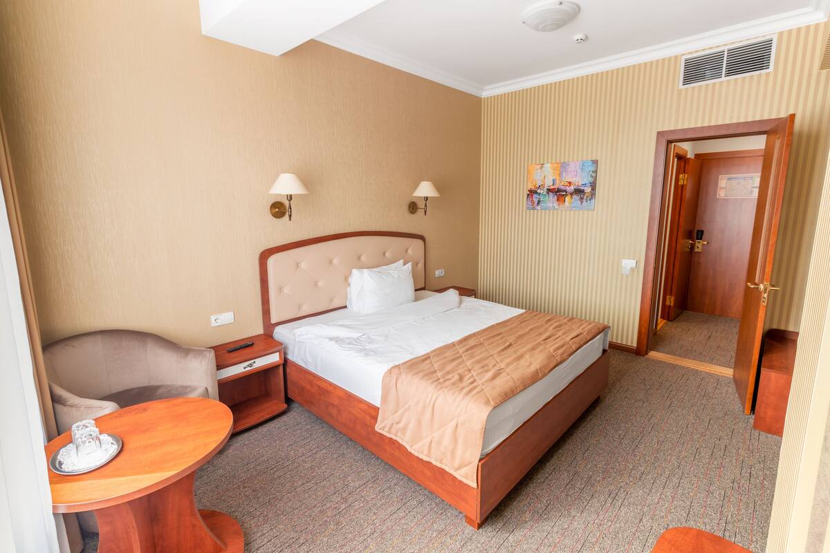 A hotel room with a bed, bedside table, chair, and a small table with a tray.