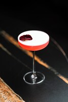 Um cocktail num copo com borda vermelha, apoiado numa superfície preta.