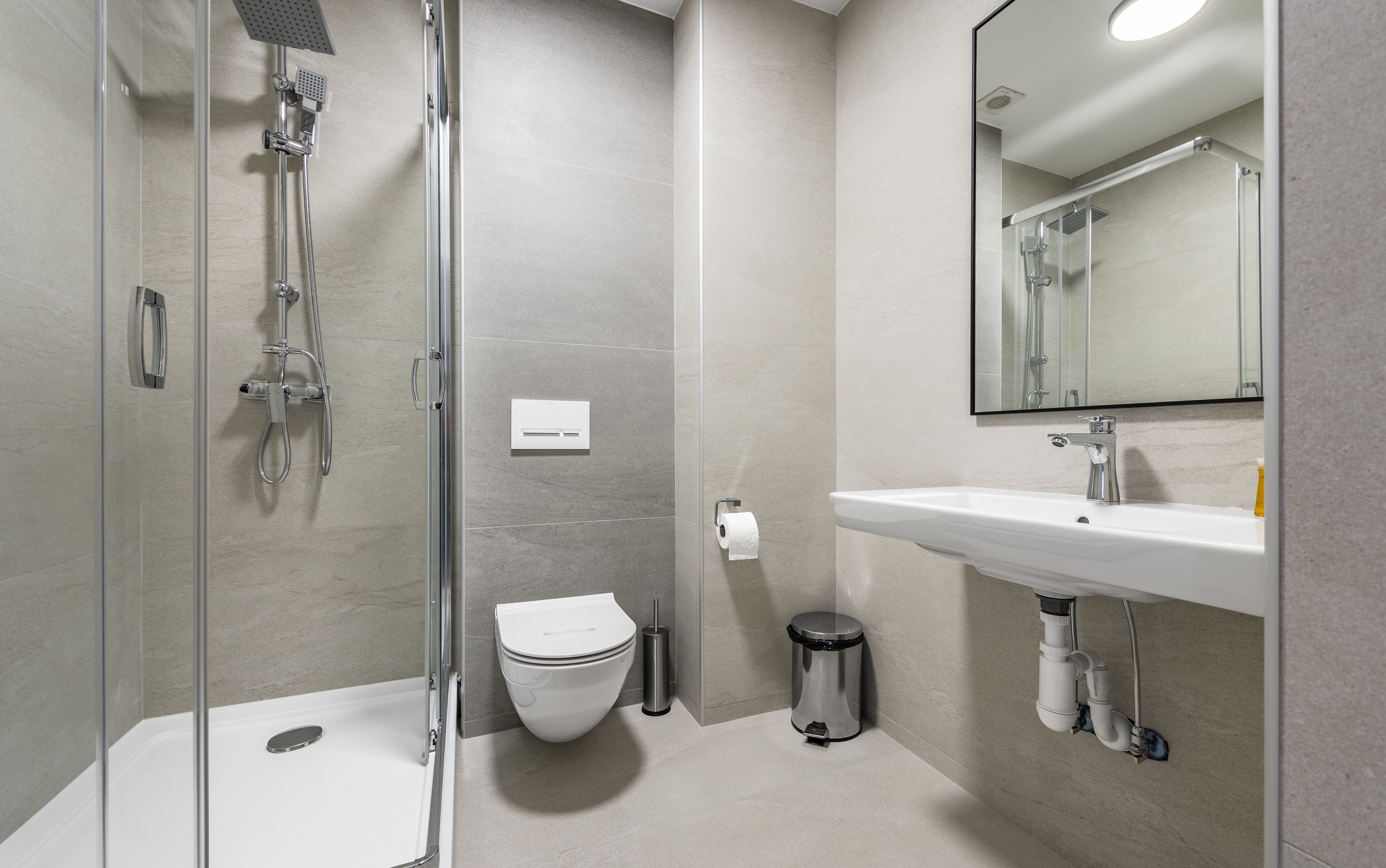A modern bathroom with a glass-enclosed shower, a toilet, a sink, and a trash can.