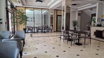 Un vestíbulo de hotel con zonas de estar, un mostrador de recepción y un amplio ventanal.