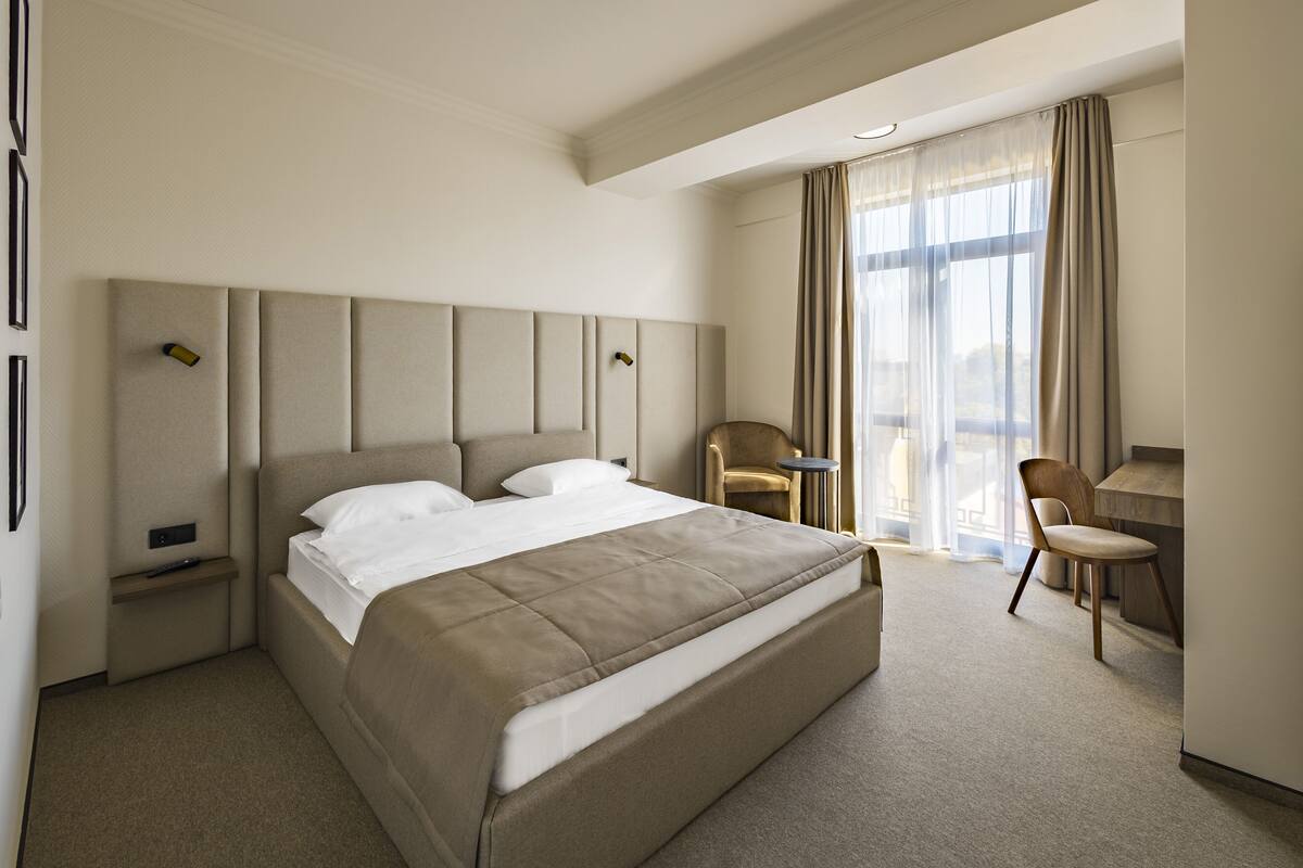 A hotel room with a large bed, a desk, and a chair.