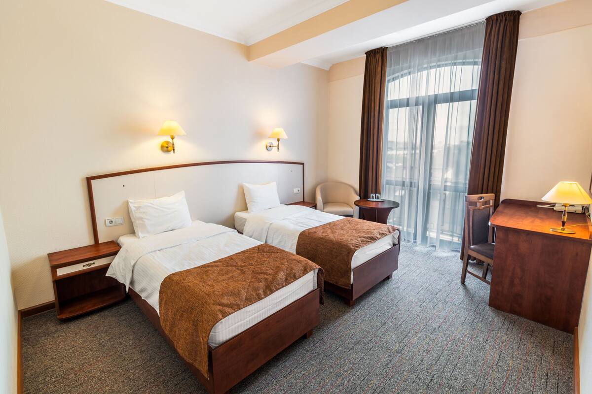 A hotel room with two beds, a desk, a chair, and a window with curtains.