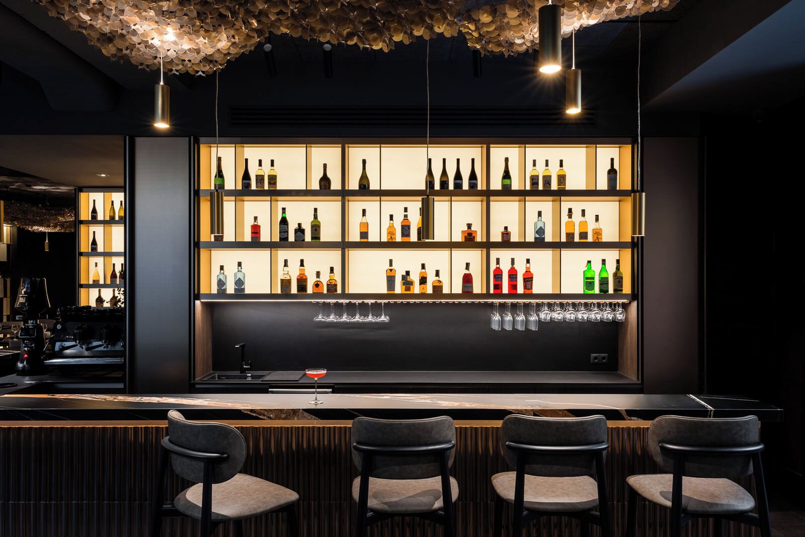 Een bar met verschillende flessen op de planken, een bargedeelte en drie stoelen.