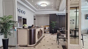 A hotel reception area with a reception desk, seating area, and a large potted plant. - Regency Hotel (Chisinau)