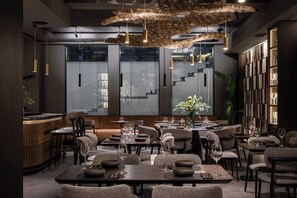 A modern restaurant interior with high ceilings, pendant lighting, and a central seating area with round tables and chairs. - Regency Hotel (Chisinau)