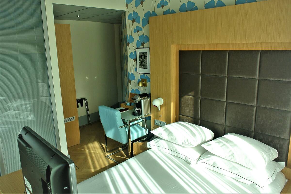 A hotel room with a bed, a desk, a chair, a lamp, and a picture on the wall.