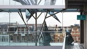 A modern glass structure with a metal framework, reflecting surrounding buildings. A sign indicates the location is the Amadi Park Hotel Reception. - Amadi Park Hotel (Amsterdam)