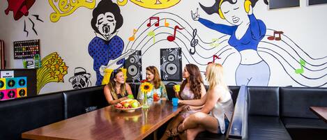 A group of people seated around a table in a room with a mural of musicians and musical notes.
