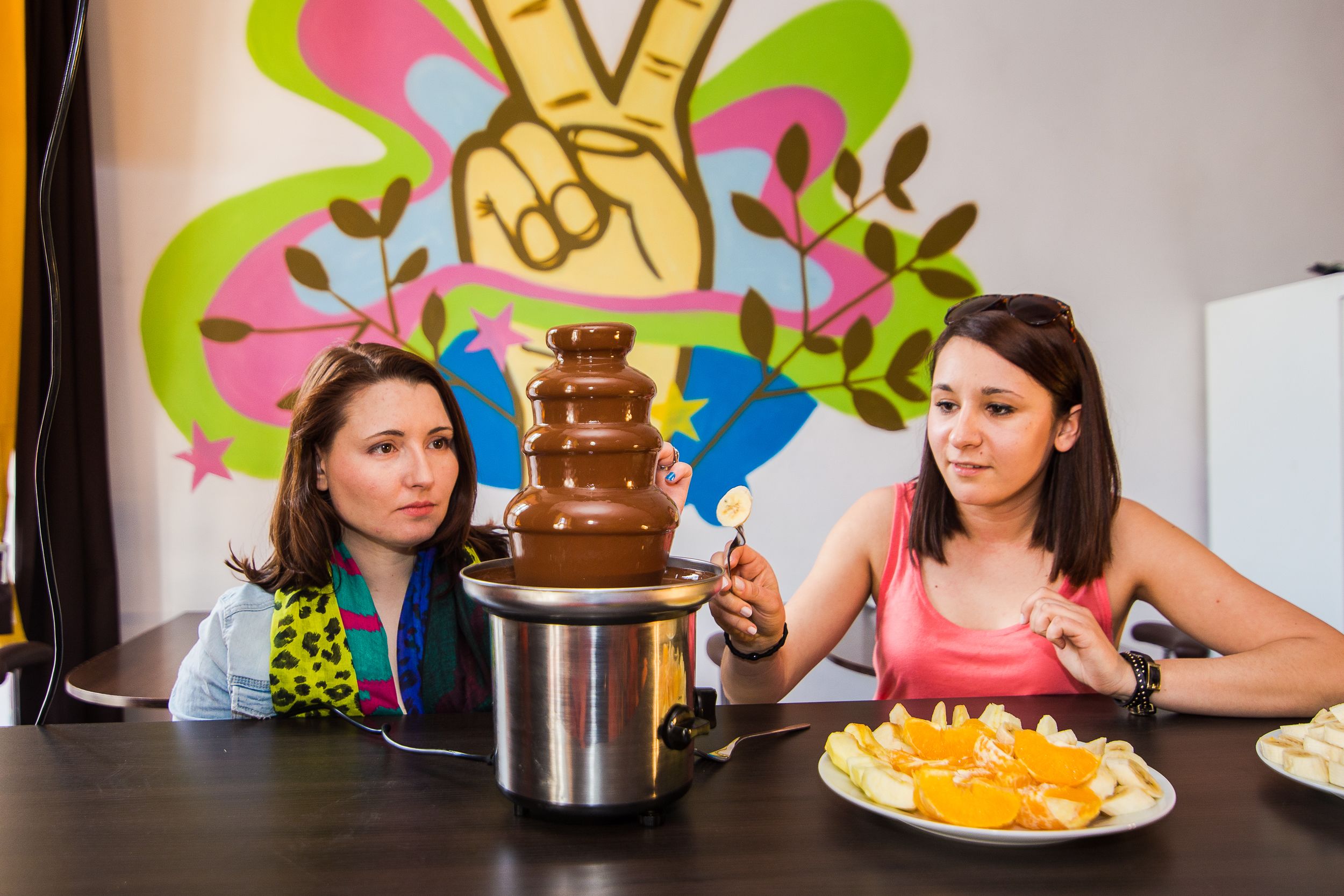 Two people sitting at a table with a chocolate fountain and plates of fruit.