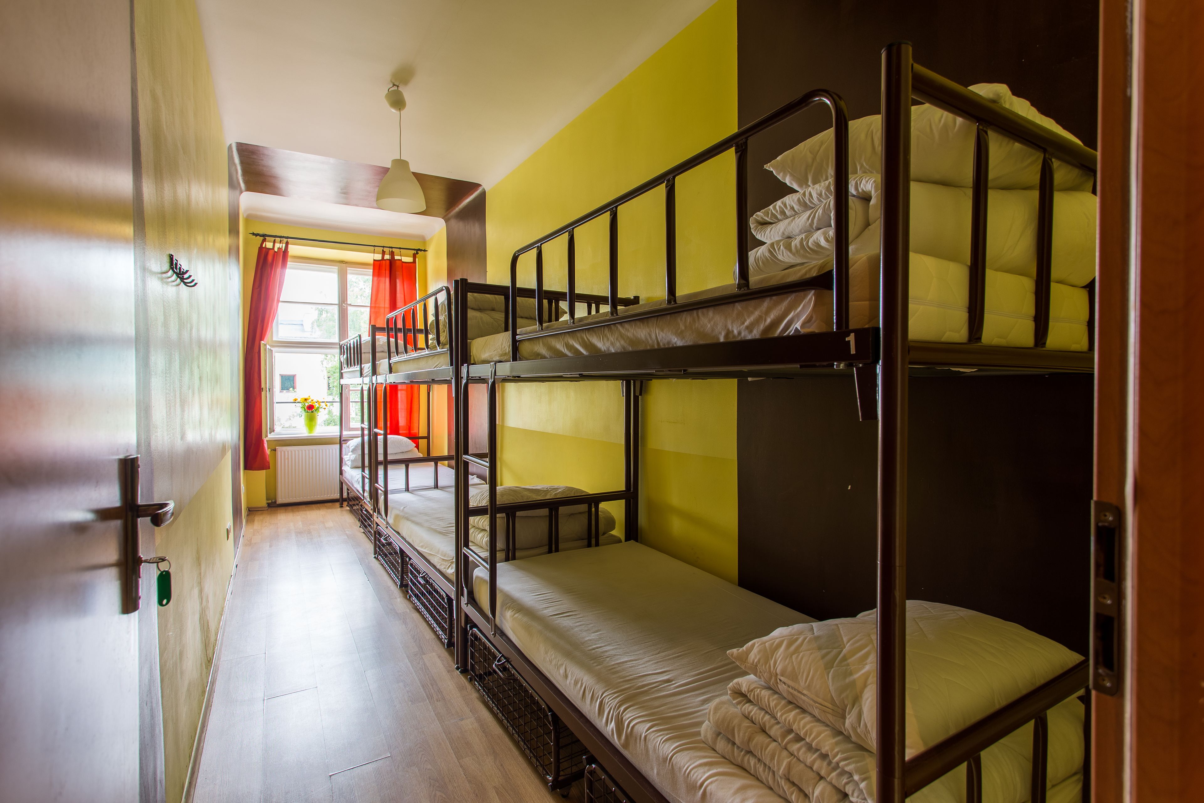A bunk bed room with wooden flooring and a window with red curtains.