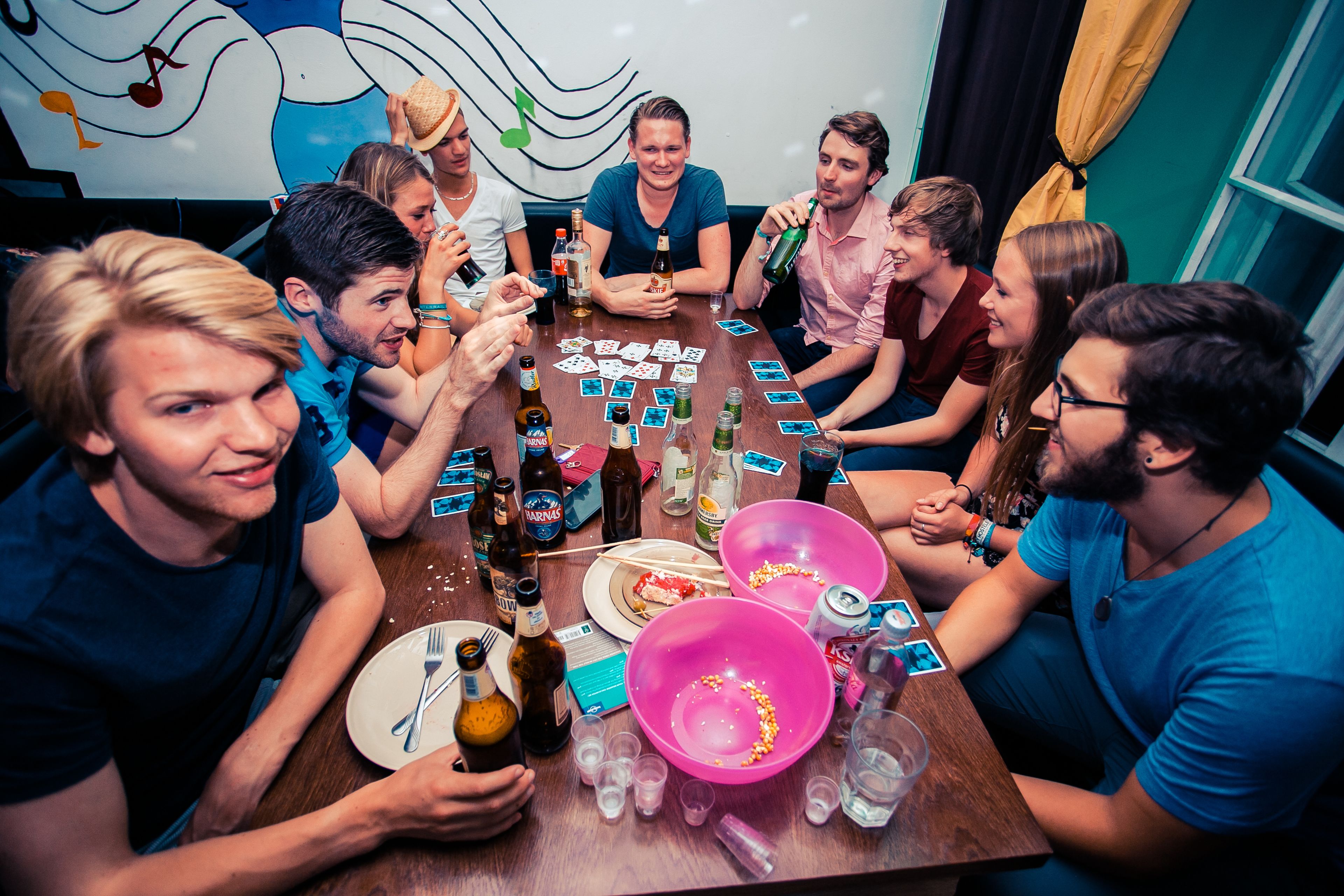 A group of people around a table with cards, bottles, and glasses, suggesting a social gathering or game night.
