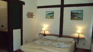 A neatly made bed with two pillows and two towels, two bedside lamps, and two paintings on the wall. - Barla Inn Suites (Búzios)