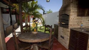 An outdoor patio with a round table and chairs, a brick oven, and a small garden with sunflowers. - Pousada Garota de Geriba (BUZIOS)