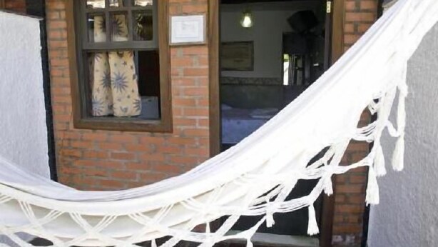 A hammock tied to a brick wall with a window and a door in the background. - Pousada Garota de Geriba (BUZIOS)
