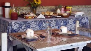 A dining table with plates, cups, and a pitcher, set against a tiled wall with a floral pattern. - Pousada Garota de Geriba (BUZIOS)