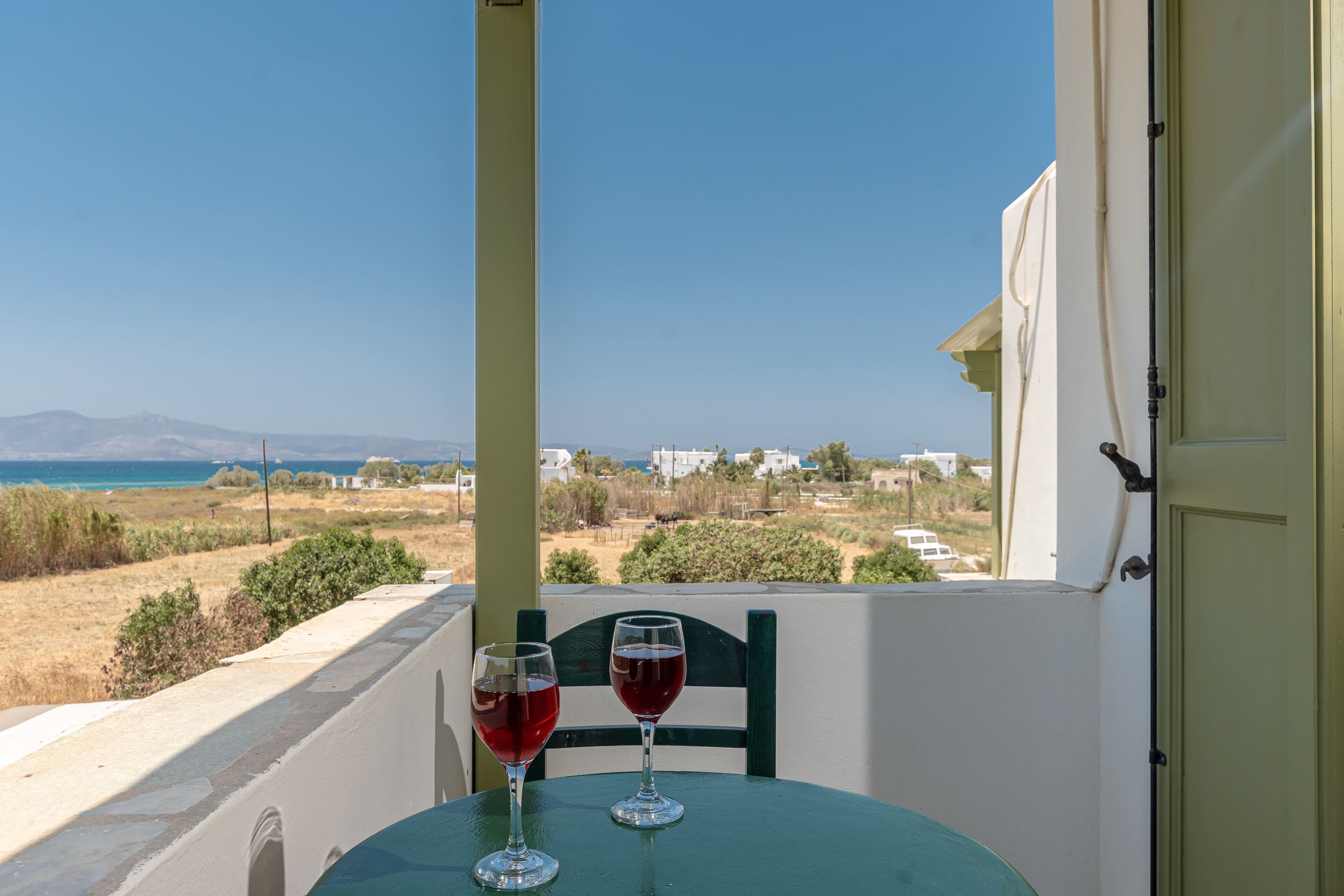 Una mesa con dos copas de vino en un balcón con vistas a un paisaje costero.