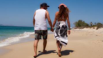 Una pareja caminando sobre una playa arenosa, con el océano al fondo.