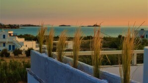 A coastal view with a sunset, grassy areas, and buildings in the background. - Studios Vrettos Beachfront Hotel (Naxos)