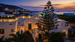 A modern white building with a green door, surrounded by greenery and a coastal view. - Studios Vrettos Beachfront Hotel (Naxos)