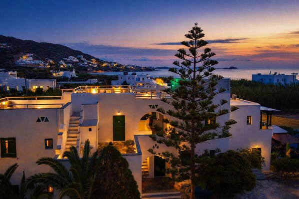 A modern white building with a green door, surrounded by greenery and a coastal view. - Studios Vrettos Beachfront Hotel (Naxos)