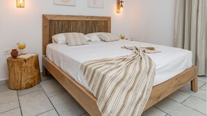 A bedroom with a wooden bed, white bedding, two wall-mounted light fixtures, and a small wooden stool with a book and a drink. - Studios Vrettos Beachfront Hotel (Naxos)