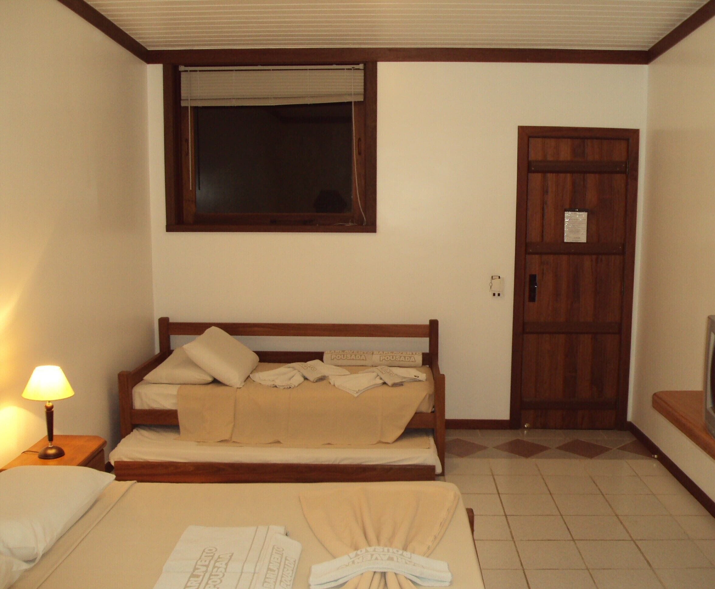 Una habitación de hotel con una cama, una lámpara de noche, una ventana y una puerta.