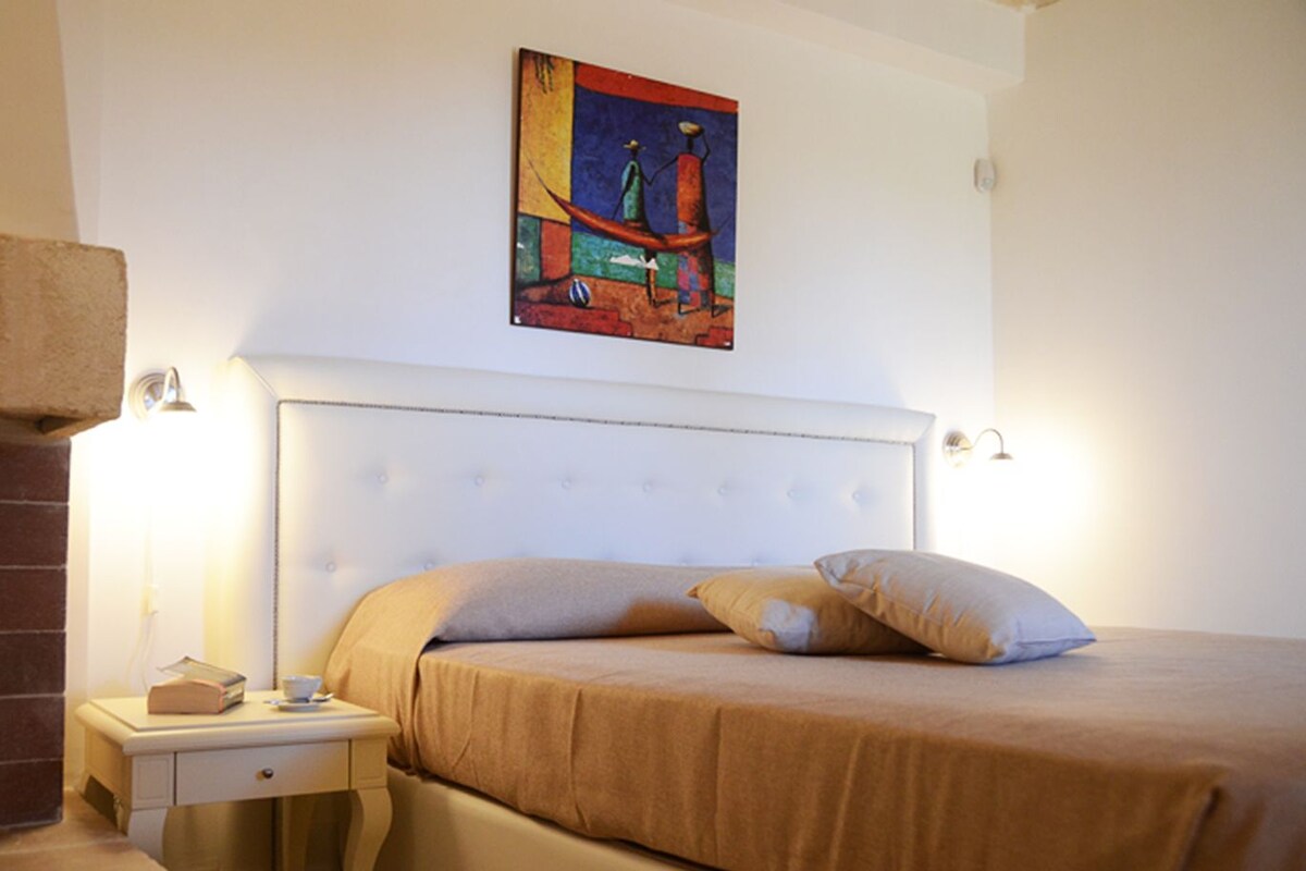 Ein Schlafzimmer mit einem weißen Bettrahmen, einem Nachttisch mit Buch und Tasse, und einem Gemälde über dem Bett.