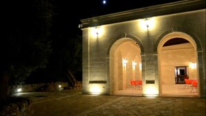 A building with arched entrances and a stone facade, illuminated by exterior lights.
