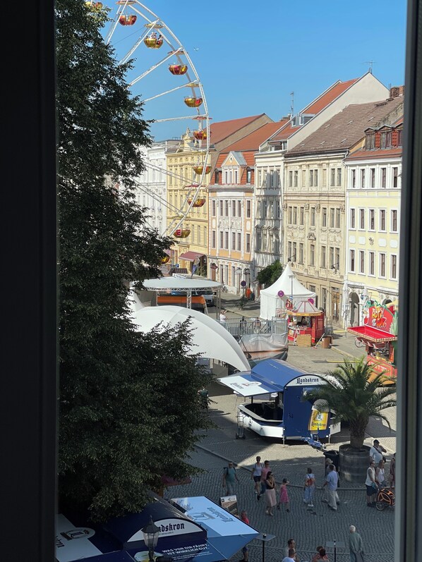 A view of a city square with a Ferris wheel, historic buildings, and a tented area.