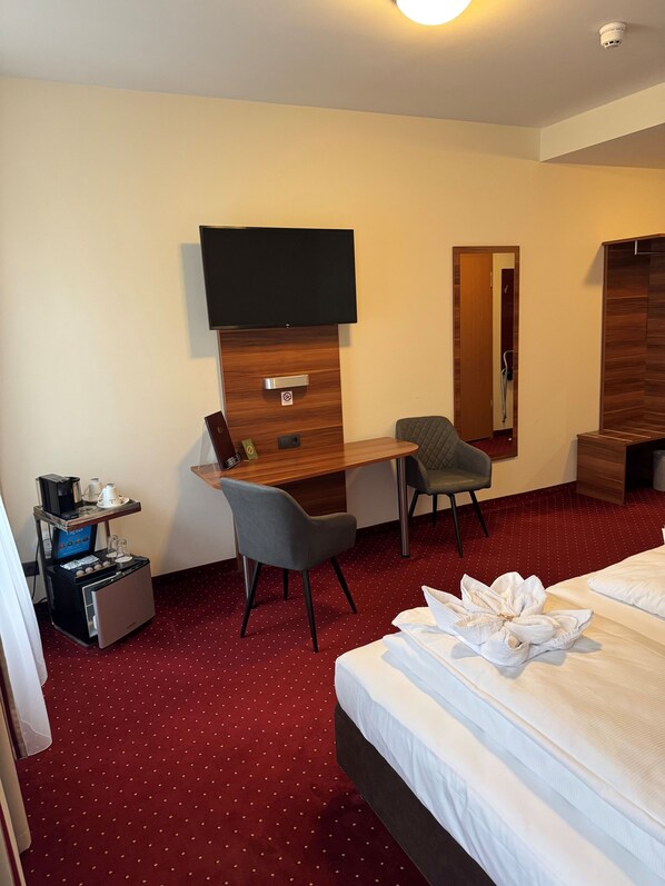 A hotel room with a bed, a desk with a chair, a television, and a coffee machine.