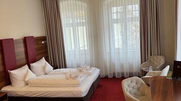A hotel room with a large bed, a desk, and a chair. There are curtains on the windows, and a ceiling light is on.