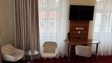Habitación de hotel con cama, dos sillas, una mesita, televisor y ventana con cortinas.