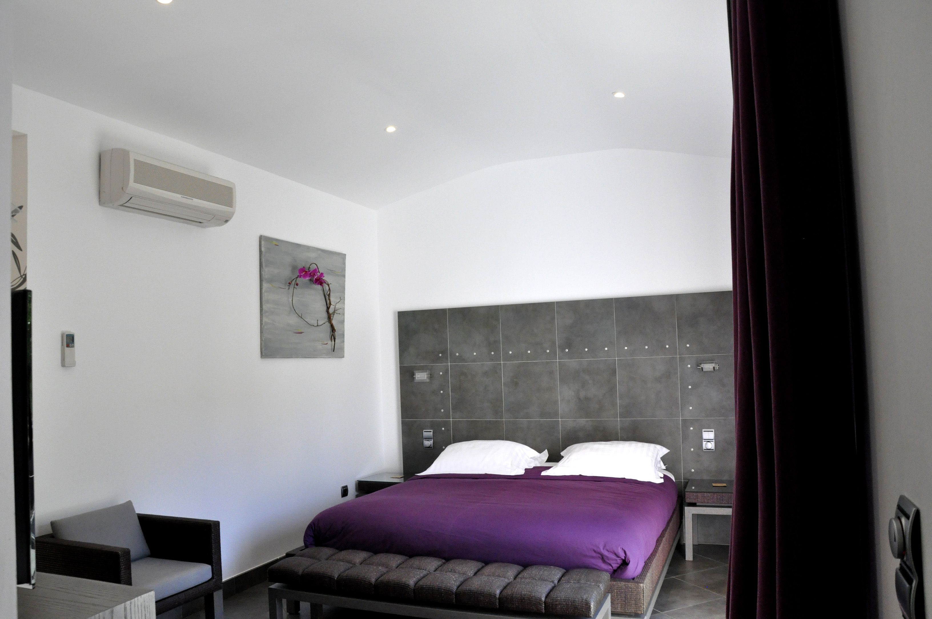 Un dormitorio moderno con una cama, un banco, una silla y un aire acondicionado instalado en la pared.