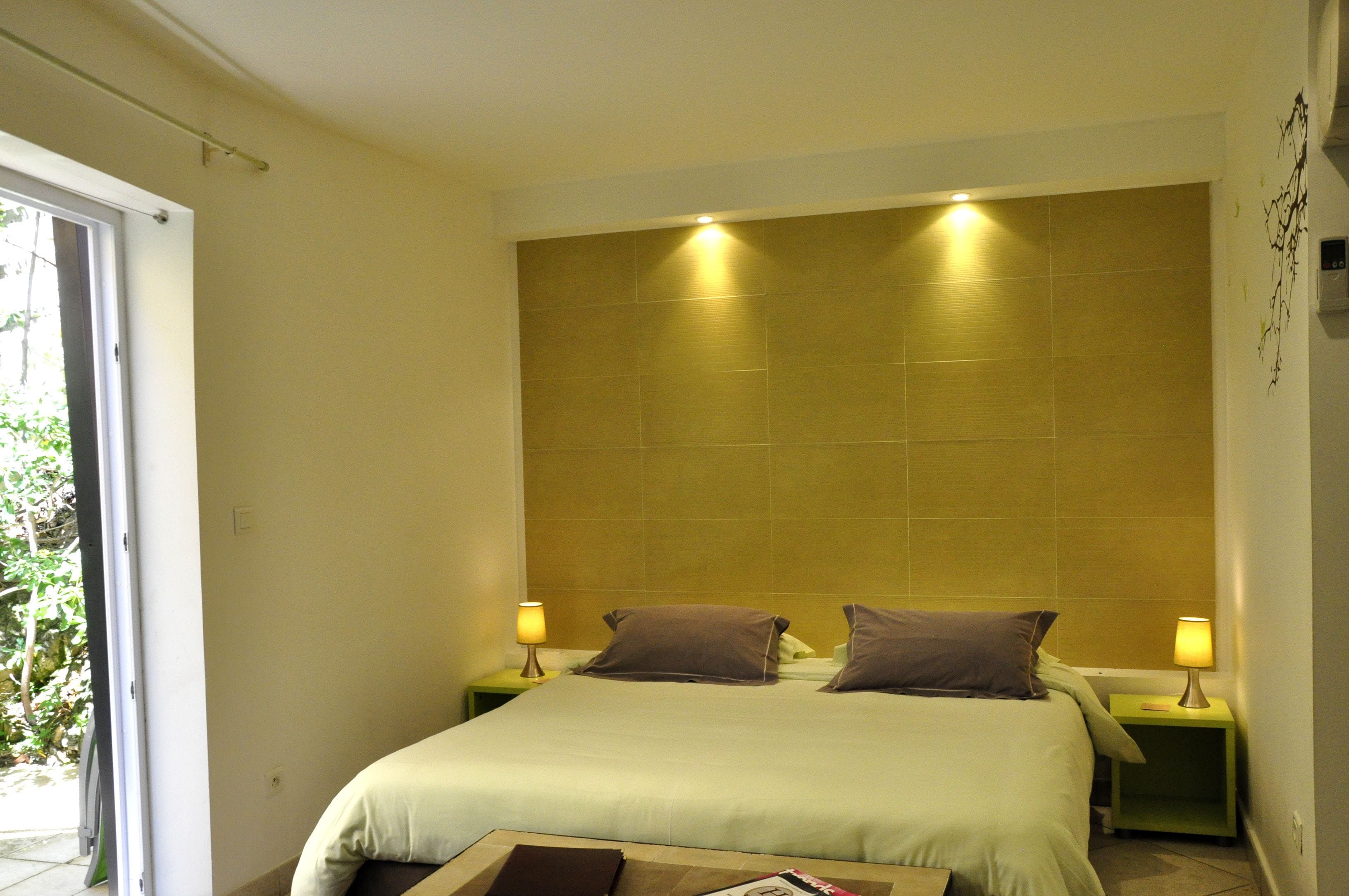 Ein Hotelzimmer mit einem großen Bett, zwei Nachttischen mit Lampen, einem Fenster mit Blick auf Grünflächen und einer Wand mit einem dekorativen Element.