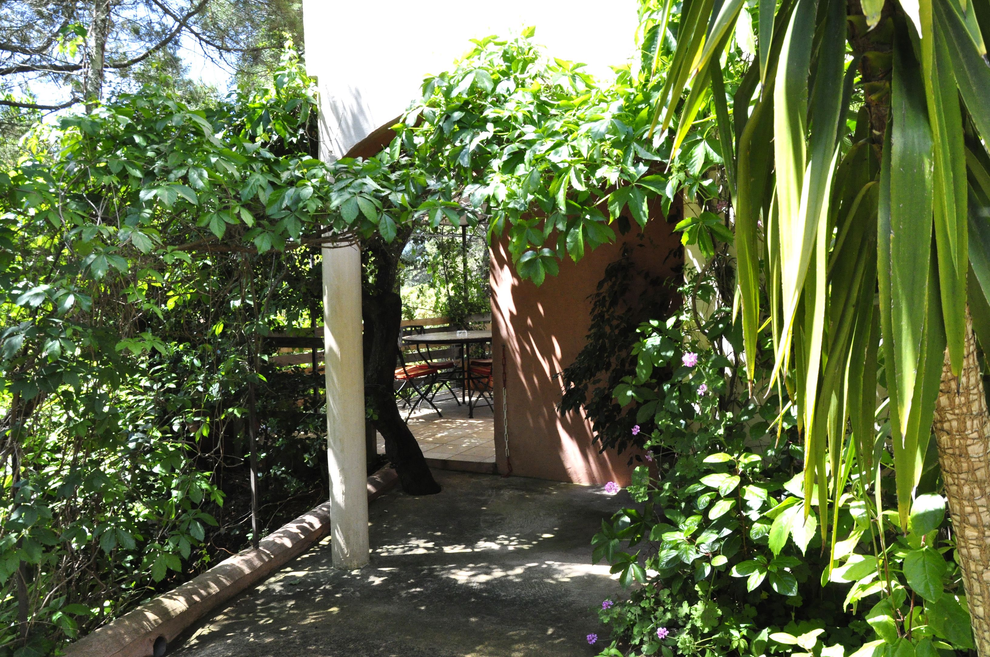 A garden pathway leading to a covered outdoor seating area with tables and chairs.