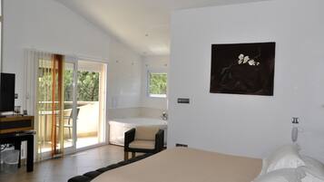 A modern bedroom with a large bed, a desk with a computer, a sliding glass door to a balcony, and a painting on the wall.