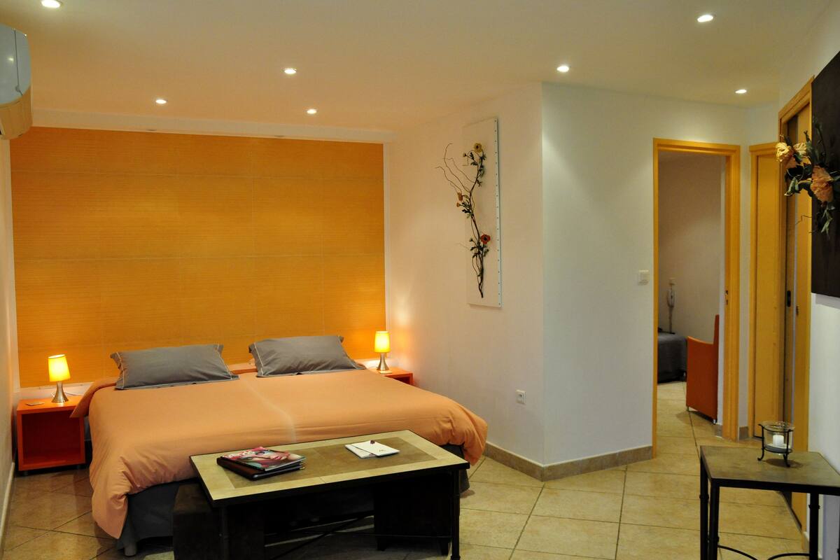 A hotel room with a bed, bedside tables, a small table, and a wall-mounted decoration.
