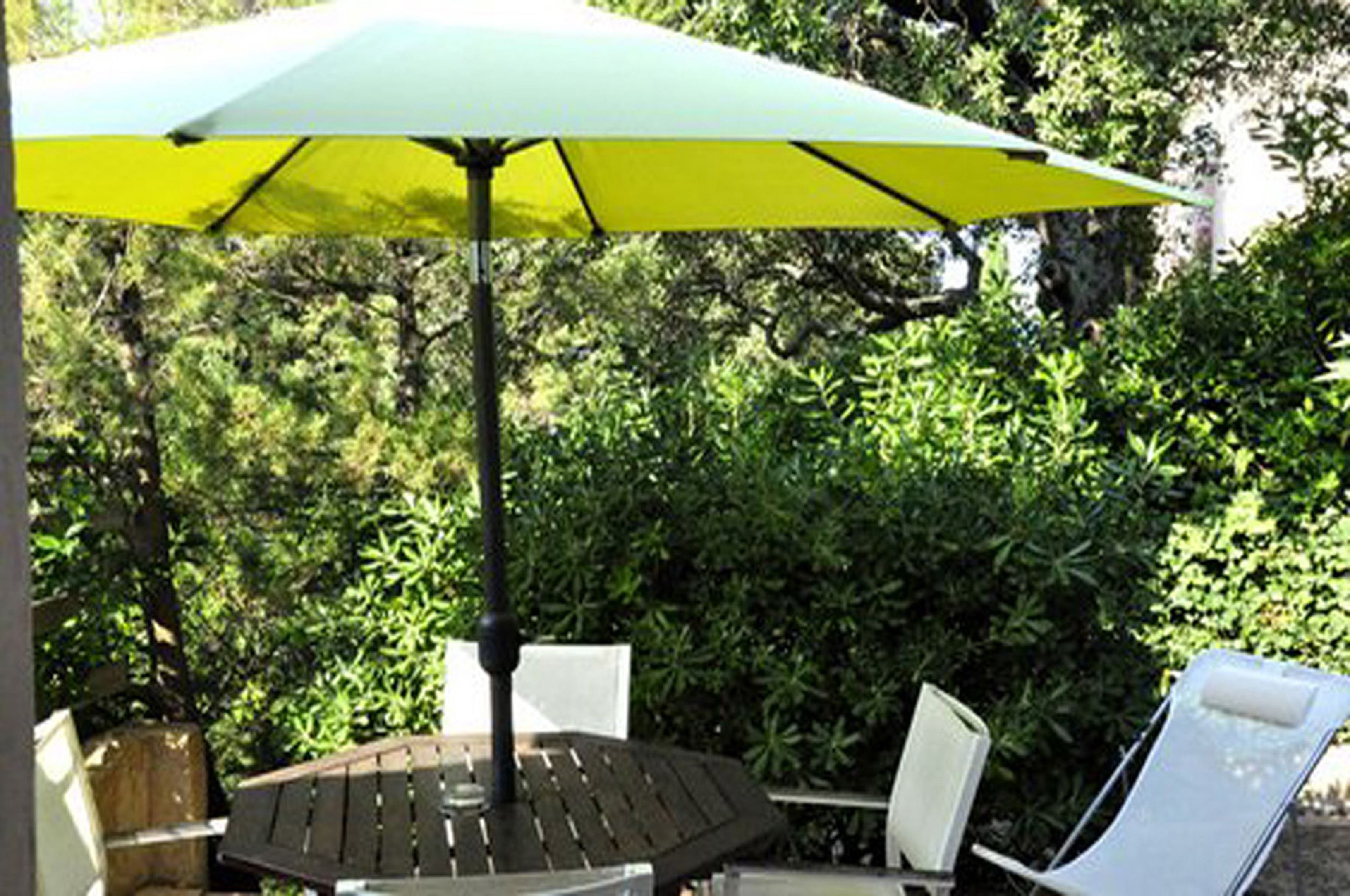 Una mesa redonda con una sombrilla verde, rodeada de sillas blancas, en un jardín.