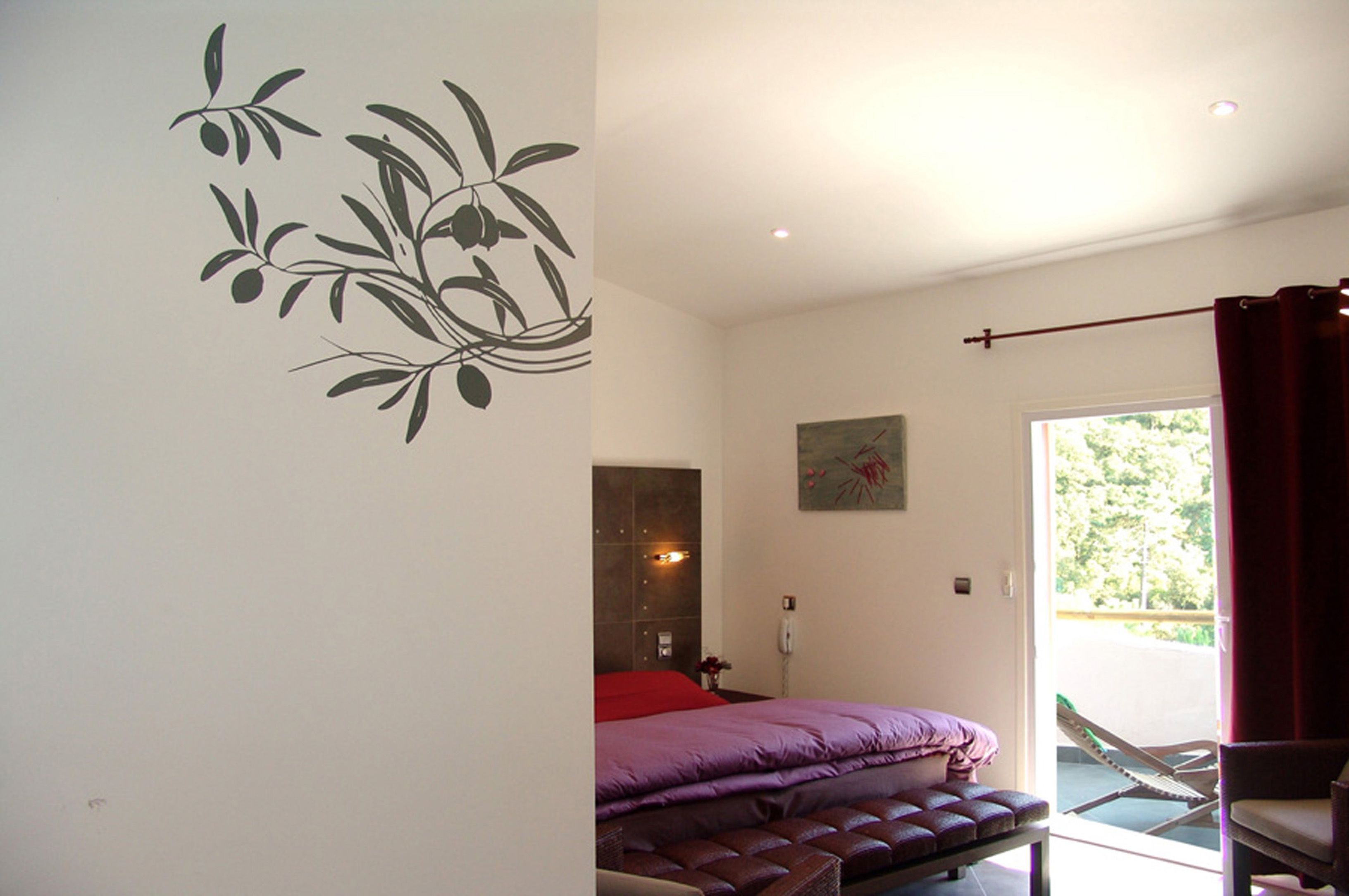 A bedroom with a bed, a bench, a wall decoration, a painting, and a view of the outdoors.