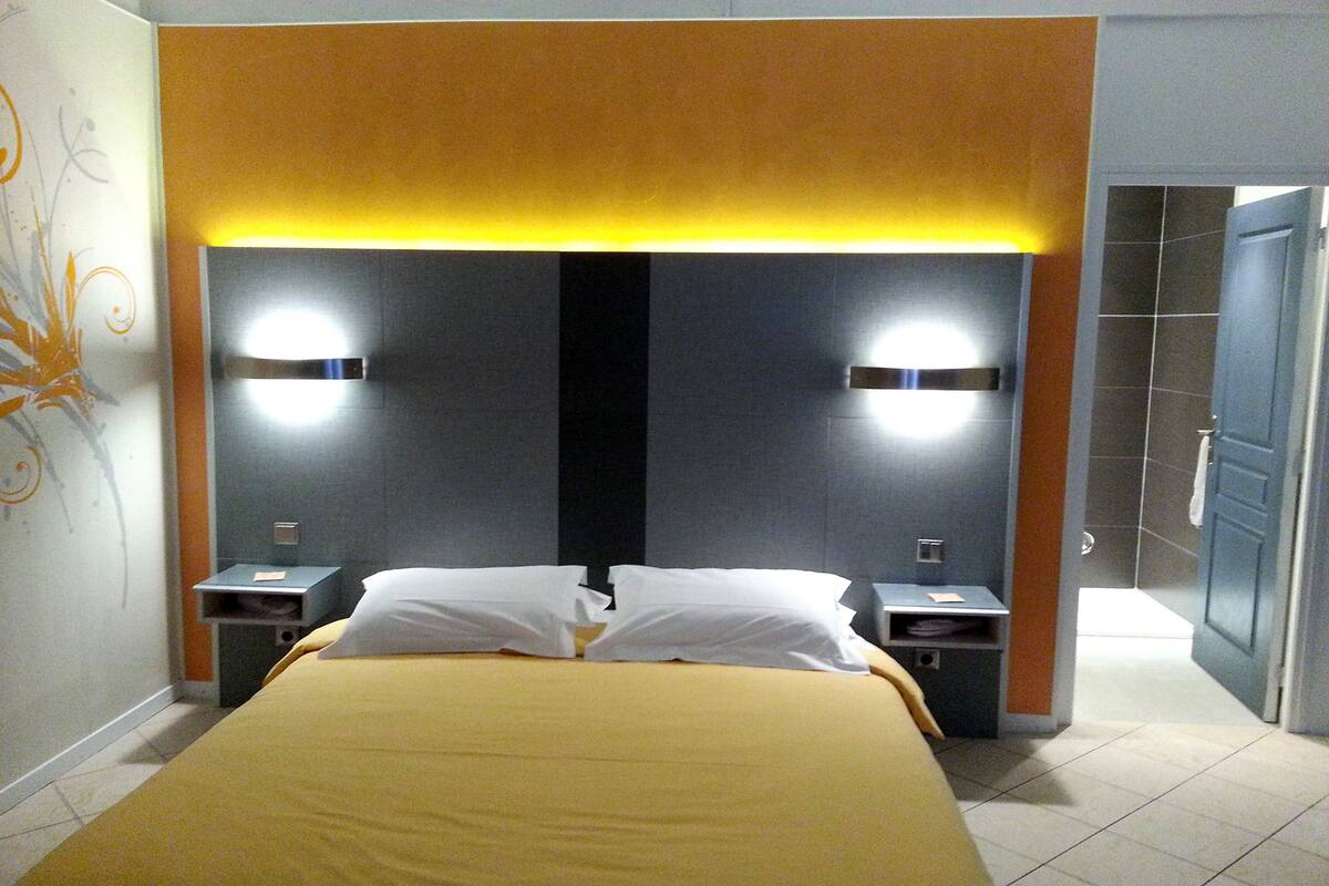 A hotel room with a large bed, two bedside tables, and a modern headboard with integrated lighting.